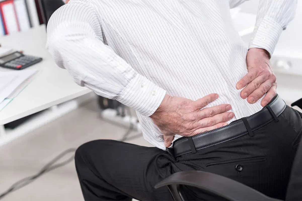 Office worker reaching for an aching lower back — degenerative disc disease treatment in Fort Wayne