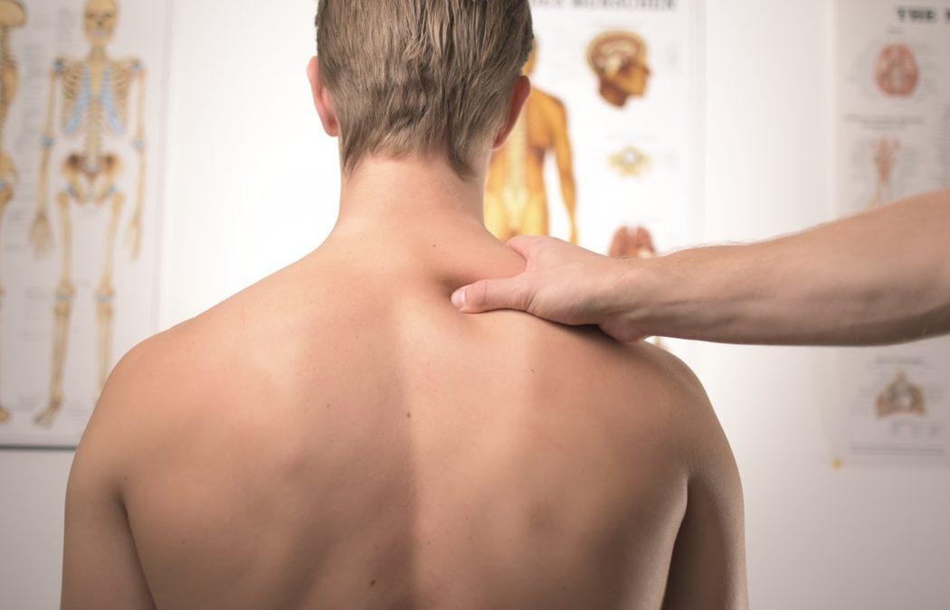 Patient receiving spinal evaluation in front of anatomy charts — herniated and bulging disc treatment in Fort Wayne
